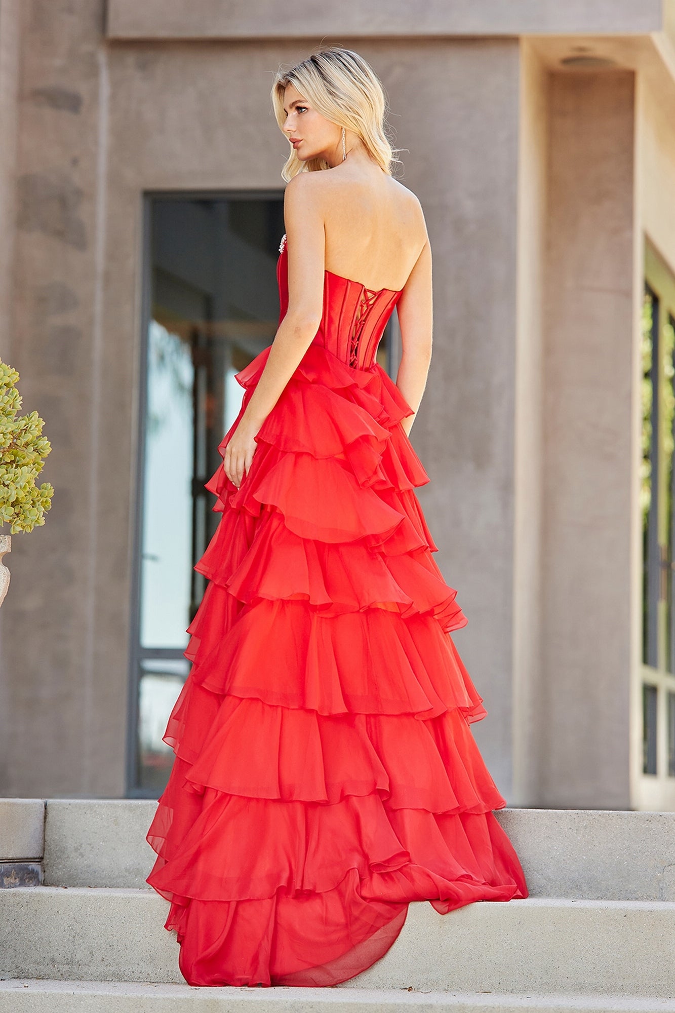 Amelia Couture 7099 prom ball gown featuring a red, strapless ruffled corset bodice with a back-lacing design and a tiered, voluminous skirt.